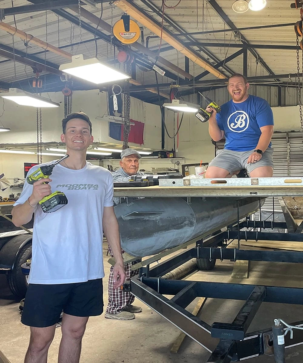 Three guys working on a pontoon boat deck in their garage