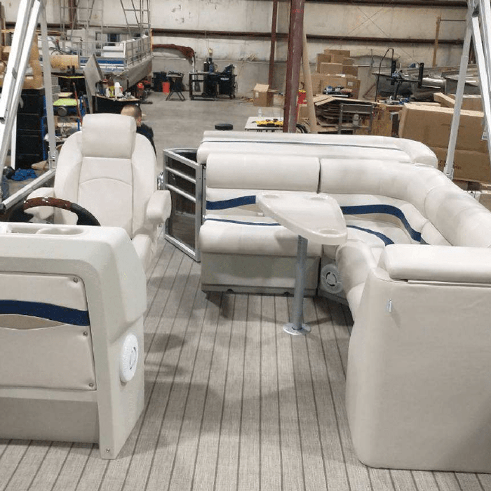 Pontoon boat inside of warehouse with corner seats, bench seats, helm chair, and console with burlwood steering wheel