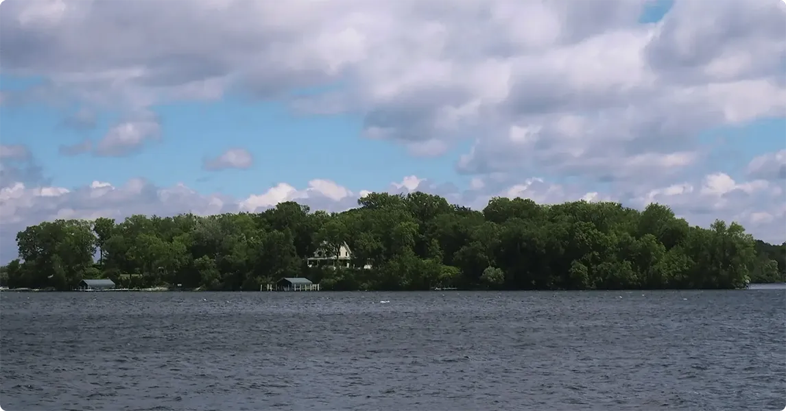 Island with trees and a house surrounded by water under a cloudy sky