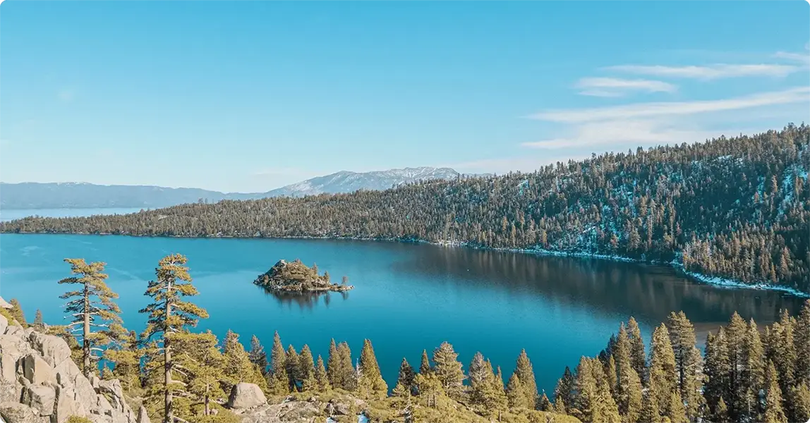 Lake with a forested shoreline under a clear blue sky.