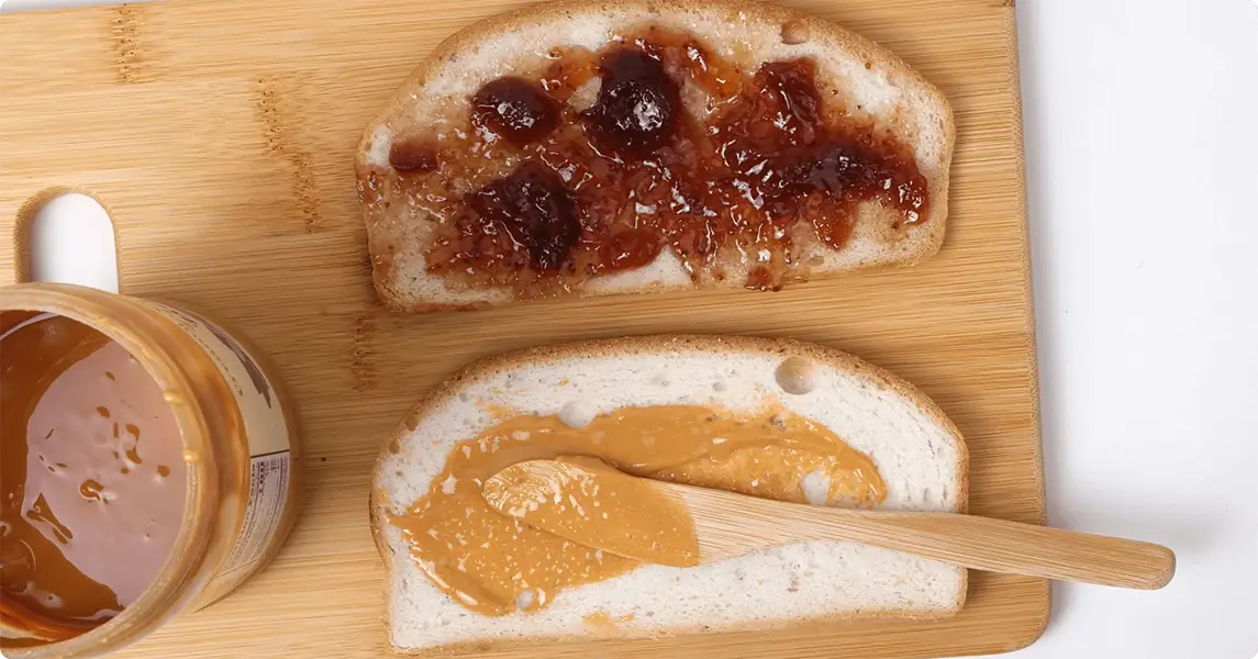 Two slices of bread with peanut butter and jelly on a wooden cutting board.